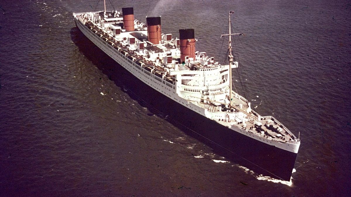 RMS Queen Mary sailing at sea in 1965, seen from above with three red funnels and a black-and-white hull.